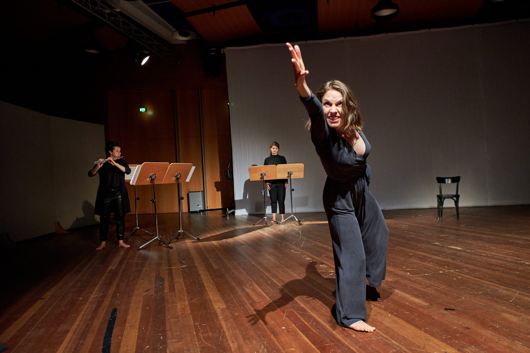 Kassandra Wedel tanzt und gebärdet im Vordergrund. Hinter ihr stehen Désirée Hall und Maren Schwier an Notenständern. Désirée Hall spielt Querflöte.