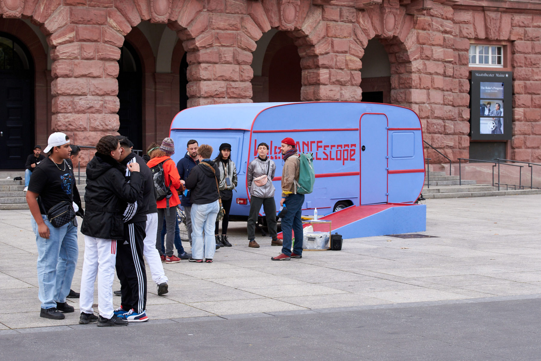 Auf dem Mainzer Gutenbergplatz steht das kaleiDANCEscope. Interessierte Passant*innen warten davor in einer Reihe stehend auf den Einlass.