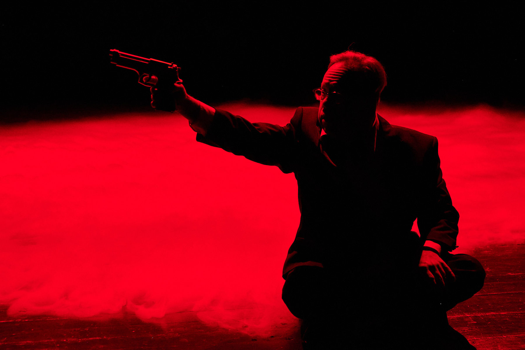 Christoph im James Bond Outfit. Nebel auf dem Boden. Alles rot beleuchtet.