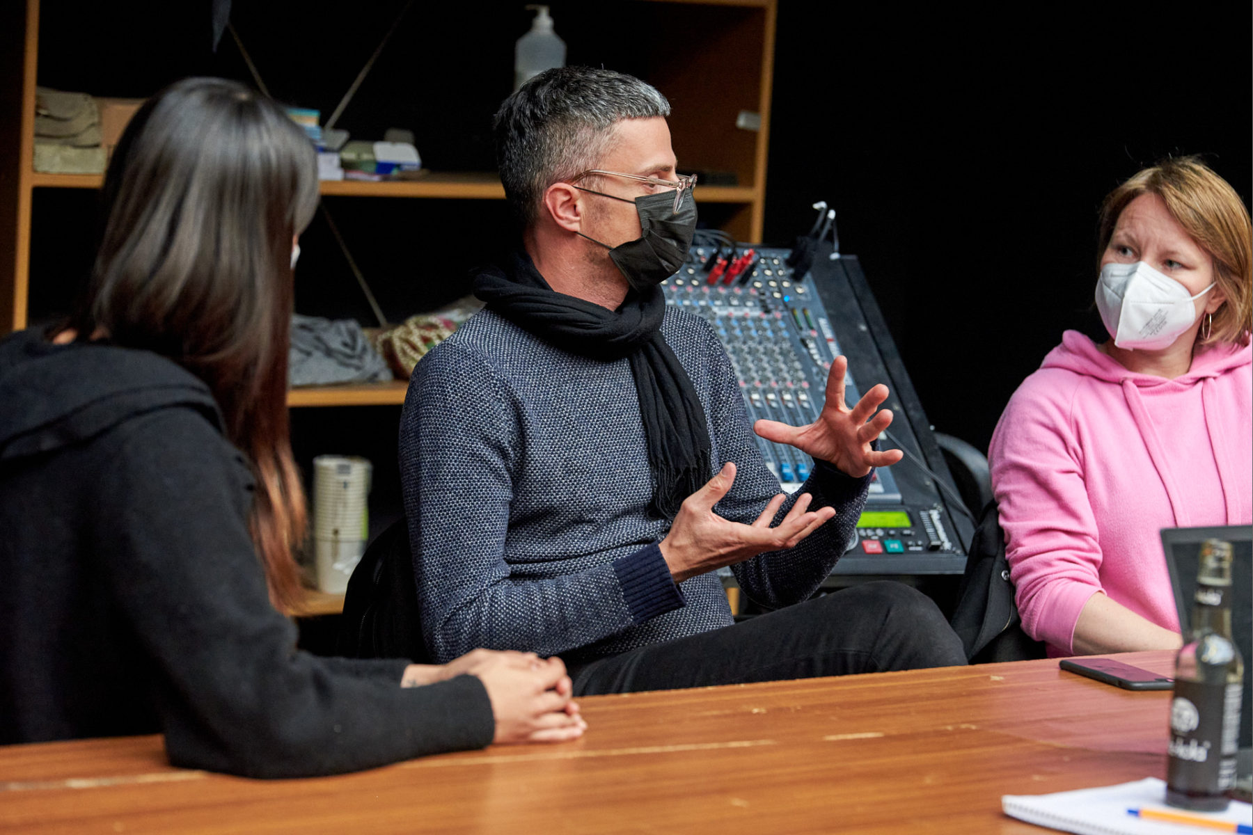 Saša Asentić sitzt an einem Tisch. Er gestikuliert und spricht mit Theresa Schütz (rechts von ihm) und Sihang Zhang (links von ihm), welche ihm aufmerksam zuhören. Sie alle tragen Masken.